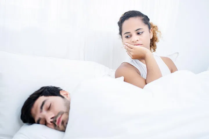Angry young woman with man sleeping in bed.