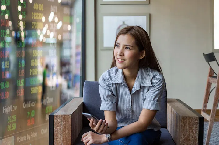 Happy asian businesswoman sitting on working space and looking the trading graph over Stock market exchange data over store blur with bokeh background in the modern Office, Business financial concept