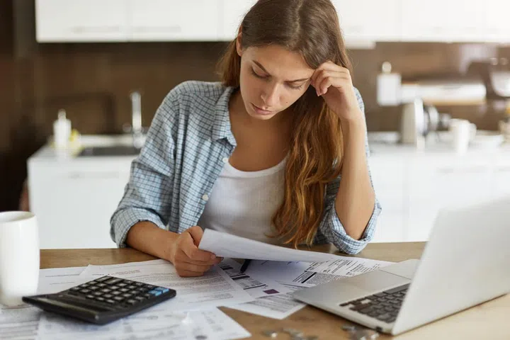 Portrait of worried young single mother feeling stressed while working through finances in kitchen late at night, thinking how to pay off debts for rent and domestic bills. Financial problems concept