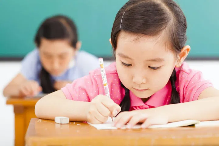 children in classroom with pen in hand