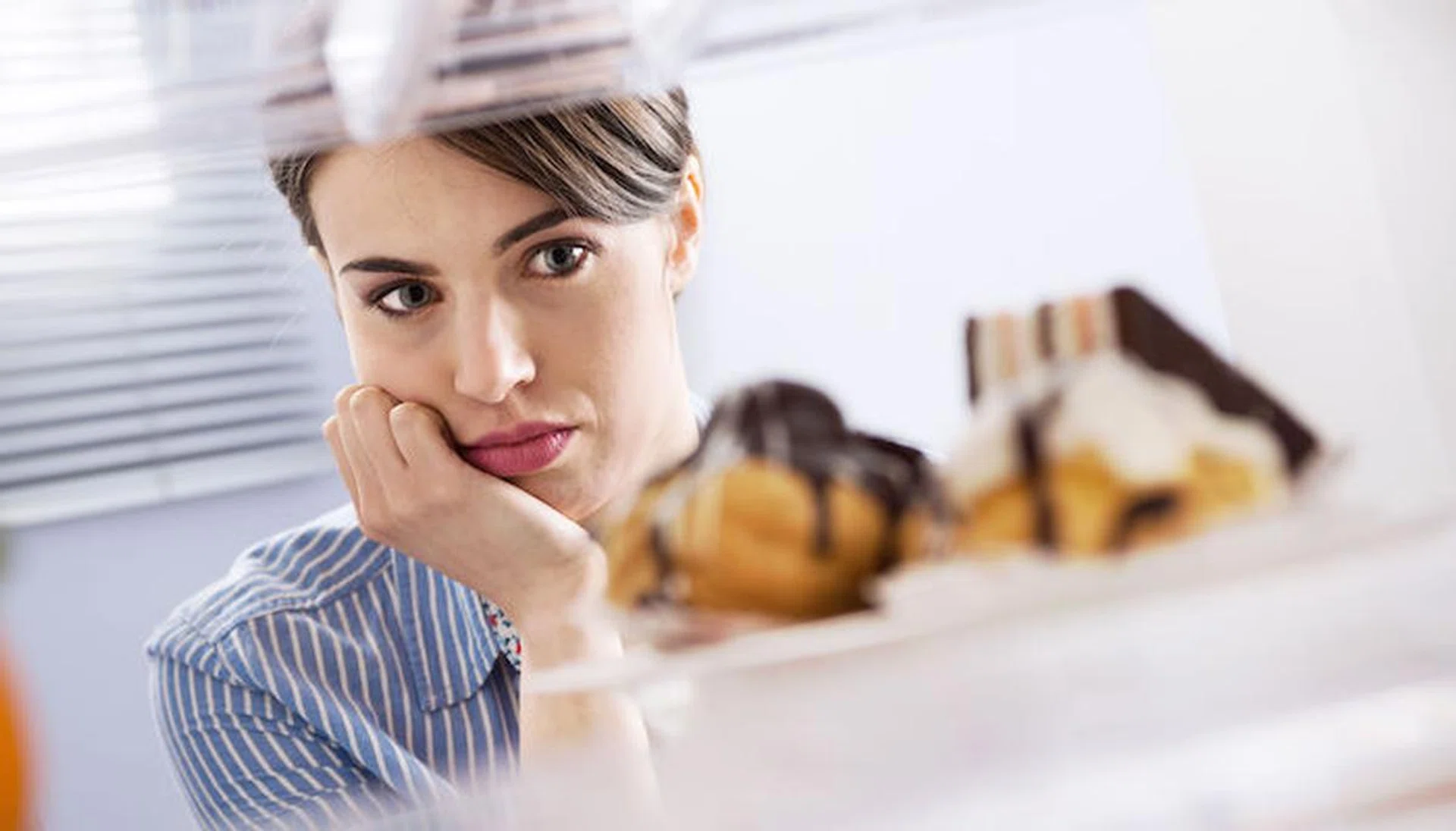 Young hungry woman in front of refrigerator craving chocolate pastries.