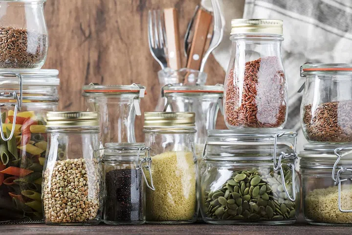 Food set. Raw cereals, pasta, groats, organic legumes and useful seeds in glass jars. Vegan source of protein and energy resources. Rustic wooden kitchen table background. 