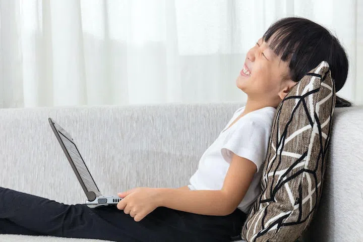 Happy Asian Chinese little girl lying on the sofa with laptop in the living room at home.