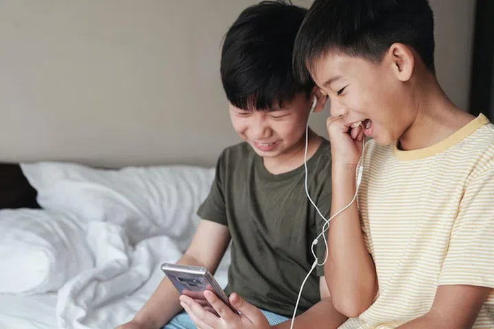 Tween boys using smartphone and sharing earphones, listening to music, watching games, using internet technology 