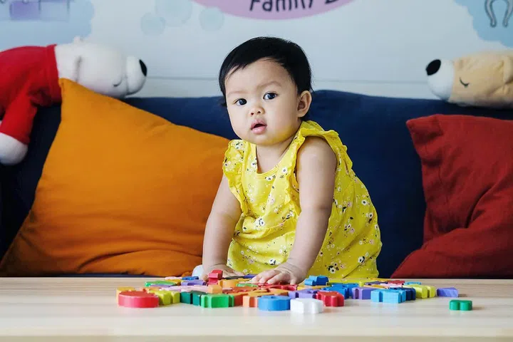 Closeup little girl play wooden jigsaw puzzle toy on sofa in the living room background