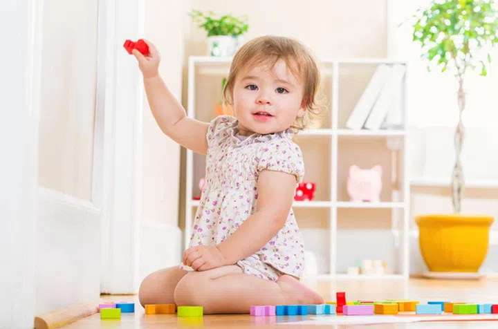 Happy toddler girl smiling and playing with her toy blocks inside her house