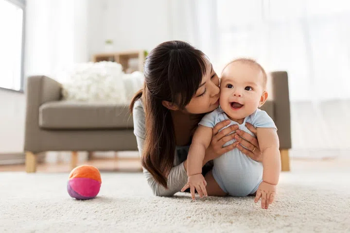 family and motherhood concept - happy smiling young asian mother kissing little baby at home