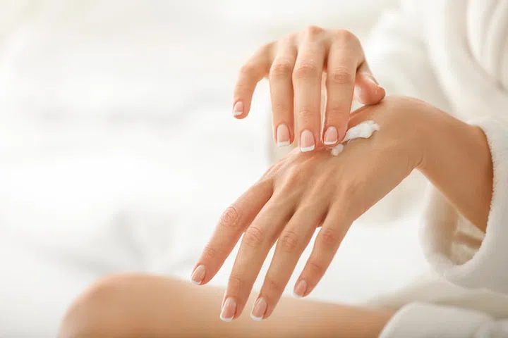 Young woman applying natural cream onto skin at home