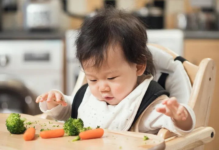 baby girl eating broccoli,carrot vegetable first time at home
