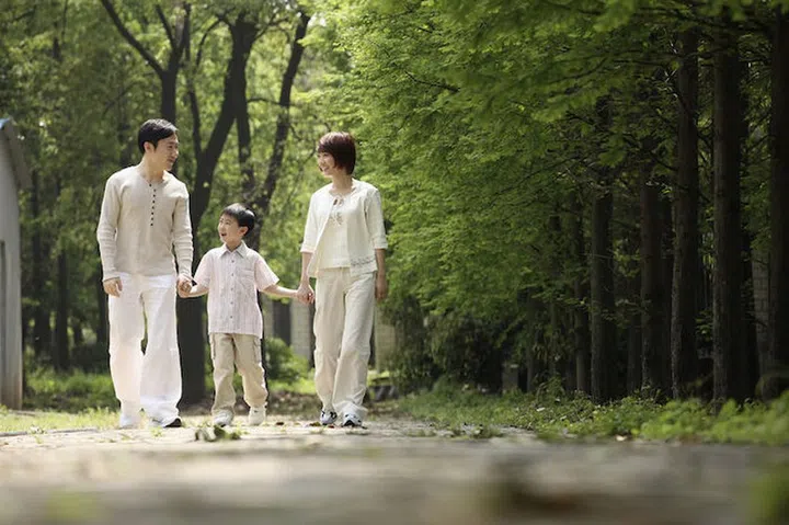 26242171 - boy holding hands with parents while walking in the park