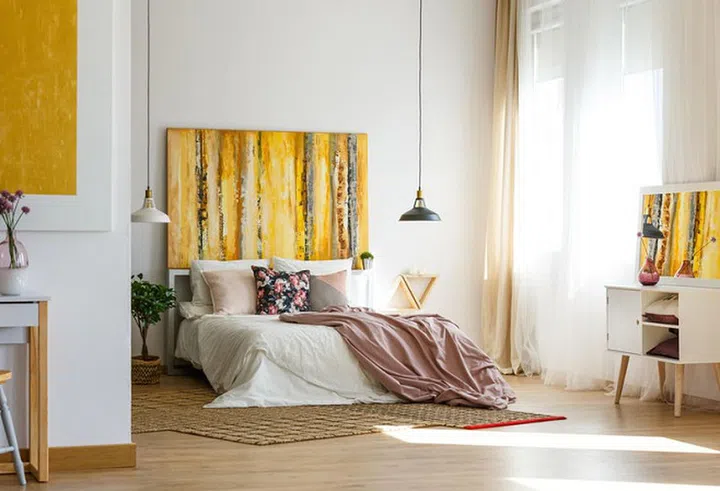 Floral pillow and pastel pink sheets on comfortable bed in contemporary bedroom interior with fancy painting on the wall