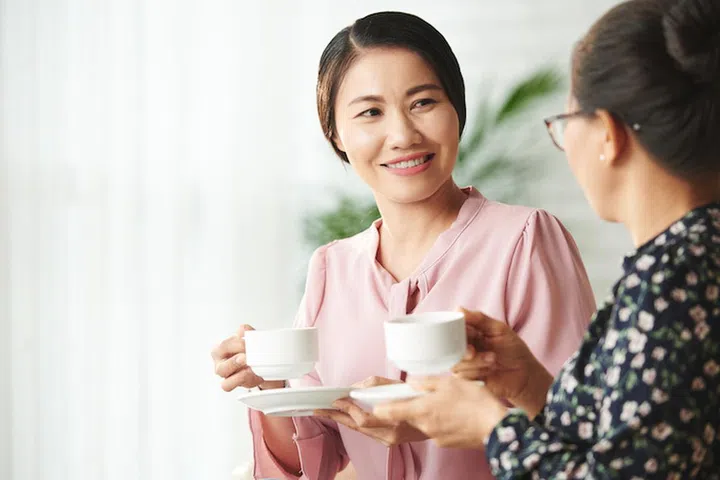 Smiling Vietnamese woman drinking coffee and chatting with her senior mother