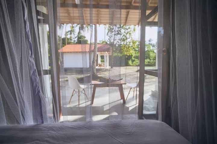 Luxury accommodation in tropical destination. Selective focus on mosquito net in bedroom of bungalow with view to garden.
