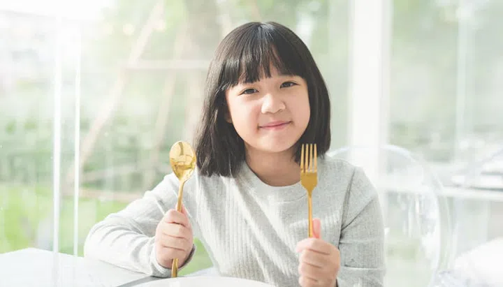Beautiful Asian girl holding a spoon and fork with empty white plate in restaurant