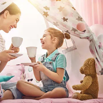 A mother and daughter having tea in a teepee tent.