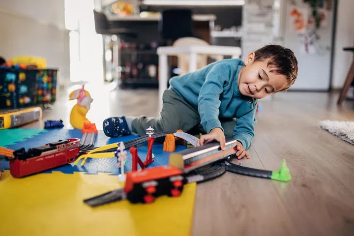 A cute three-year-old mixed-race boy is playing with toys on the floor in the apartment.