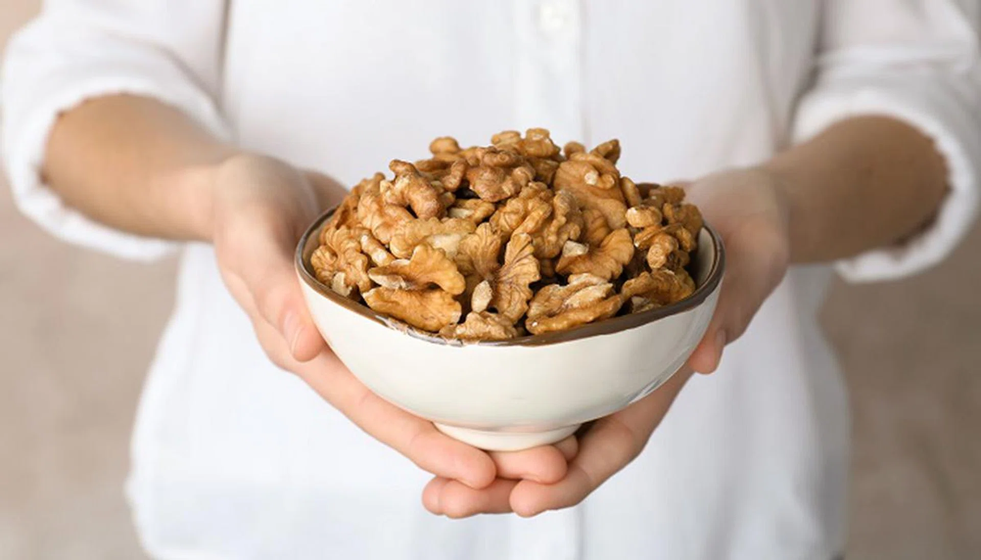 Woman holding bowl with tasty walnuts, closeup