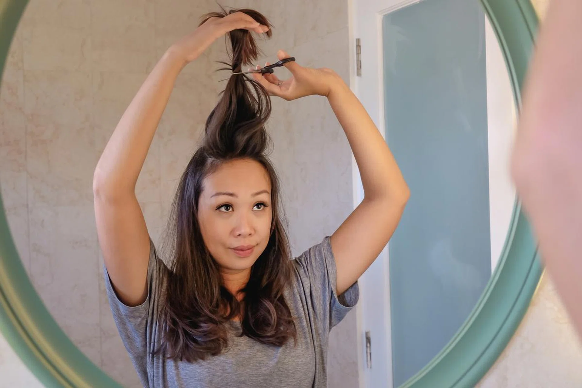 Shot of an attractive Chinese woman , lifting her hair up, while preparing to cut her hair with scissors at home during Covid 19 quarantine