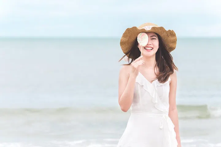 Asian woman on white dress standing over the blue sea and sky, feeling relaxing and happy on vacation in summer holiday