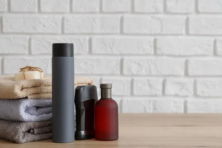 Stack of towels and male toiletries on wooden table. Shampoo, soap, bottle, deodprant and perfume bottles