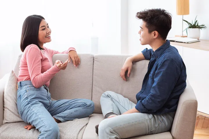 Dating Asian Couple Talking And Flirting Enjoying Conversation Sitting On Couch In Living Room At Home On Weekend. Romantic Relationship And Flirt Communication, Stay-At-Home Date Concept