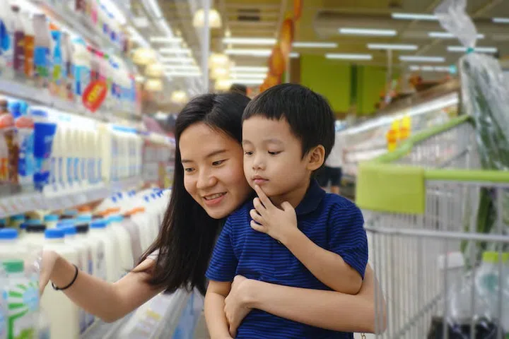 Young Asian mother and her kid shopping in supermarket with blurry background
