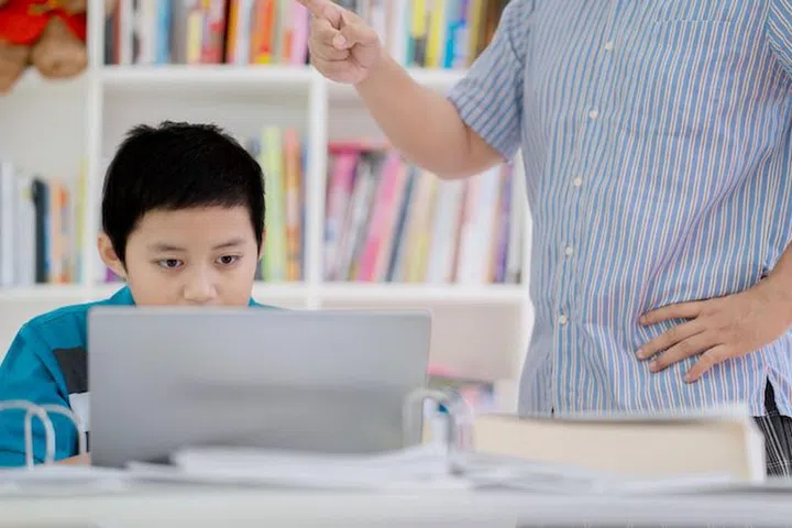 Picture of a preteen boy student being rebuked by his teacher while playing a laptop in the library