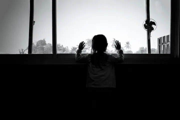 Asian child girls are standing in the dark, looking out the window,sad mood, black and white tones.