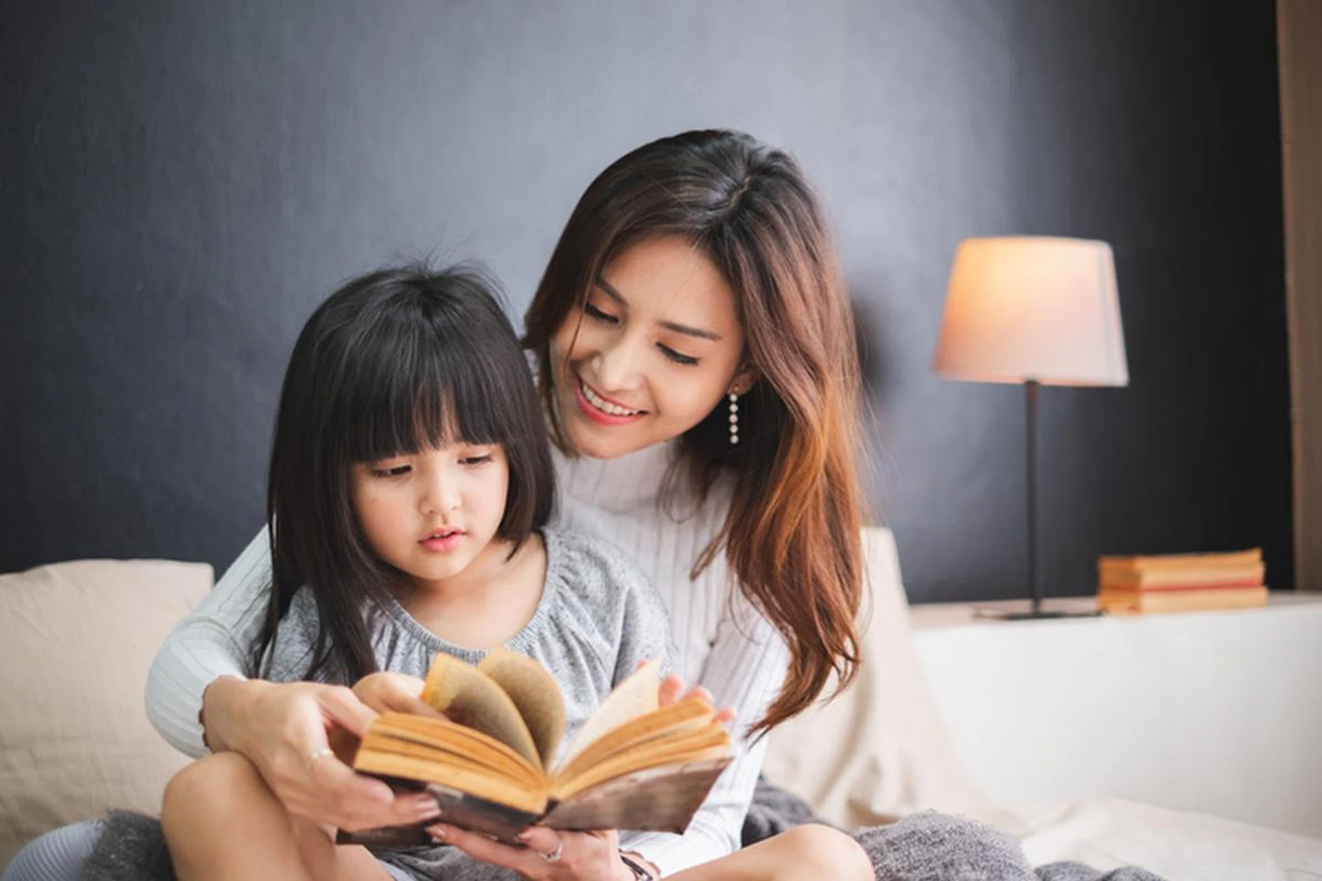 Happy Asian family mother and daughter on bed in bedroom say good night before sleep
