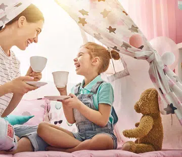 A mother and daughter having tea in a teepee tent.