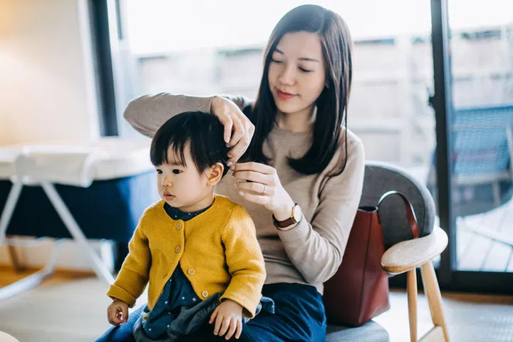Young Asian mother tying hair of little daughter and getting dressed at home before heading out. Family lifestyle