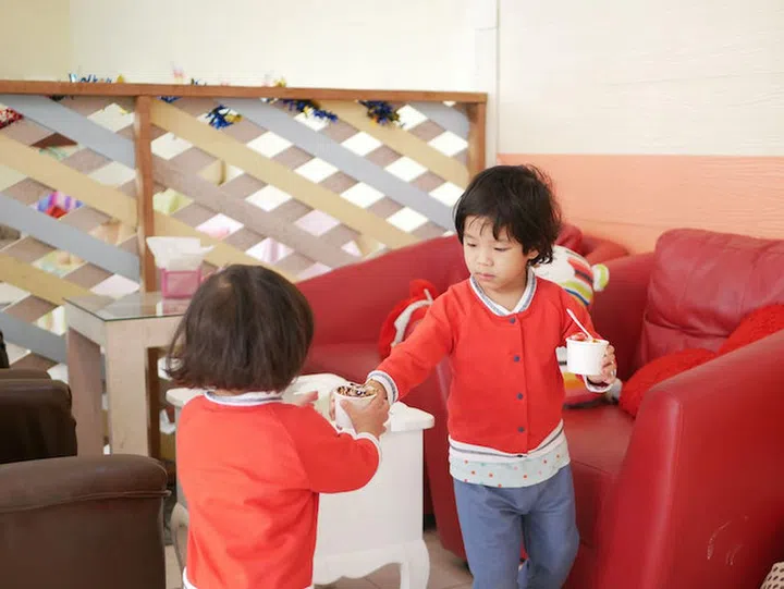 Little Asian baby girl, 26 months old, giving / sharing a cup of ice cream to her younger sister - let your kid learns to share when possible