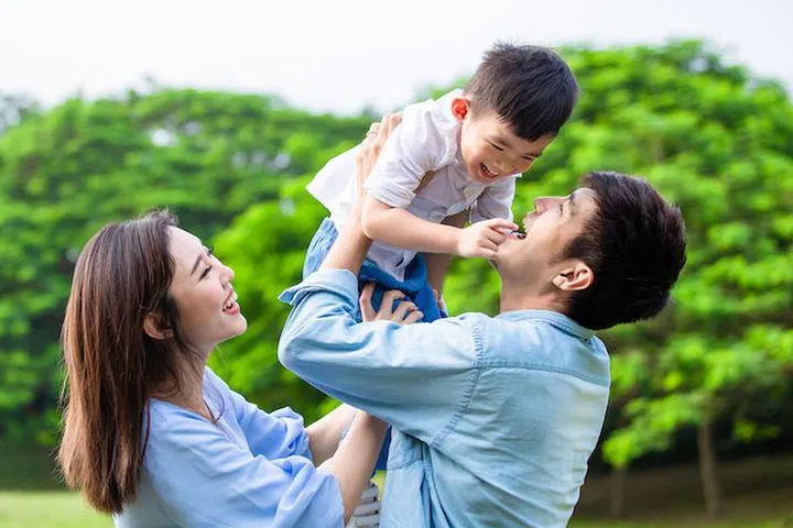 Father hold boy in his arm and parents play with kid outdoor