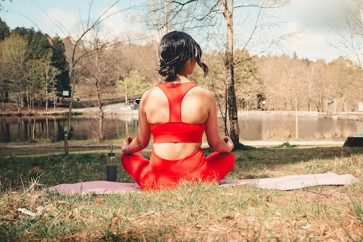 Young woman in fitness clothes doing yoga exercises over a yoga mat at the park during a sunny day