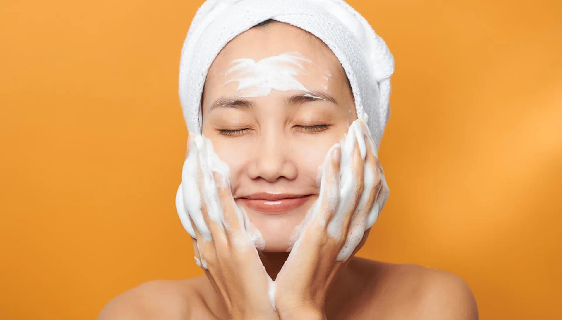 Beautiful model applying cosmetic cream treatment on her face on orange background