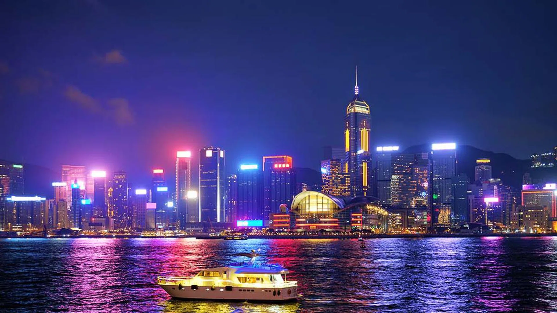 Hong Kong skyline cityscape downtown skyscrapers over Victoria Harbour in the evening illuminated with tourist boat ferries . Hong Kong, China