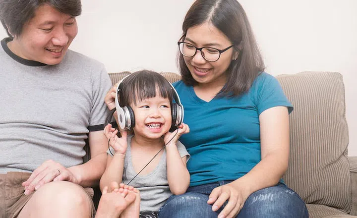 Asian parents and baby girl in sofa using tablet and headphones