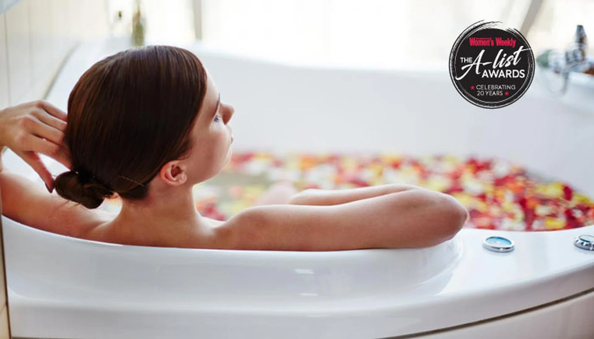 Relaxed woman sitting in bath with rose petals