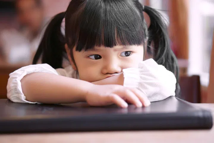 Asian children cute or kid girl upset or angry and sad feel on book and wood table with window side at home on vintage style and soft focus