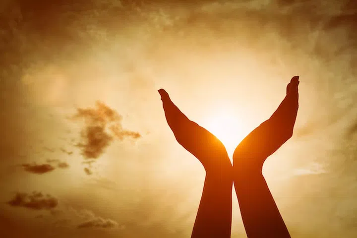 Raised hands catching sun on sunset sky. Concept of spirituality, wellbeing, positive energy etc.