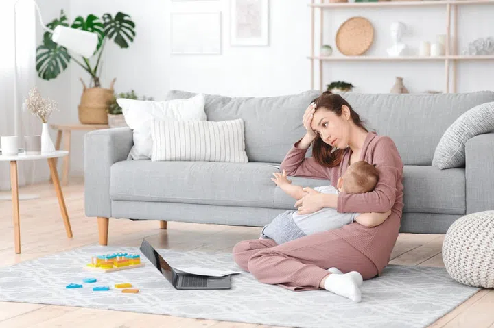 Motherhood Exhaustion Concept. Tired young mom breastfeeding baby and working on laptop at home, feeling frustrated, free space