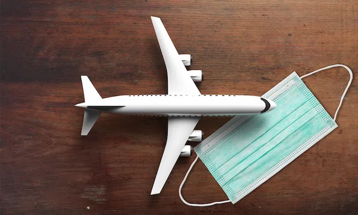 Plane on a COVID 19 protective face mask, wooden background. Airplane flight safe, protection against coronavirus. Travel tourism new normal, cancelled flights concept. 3d illustration