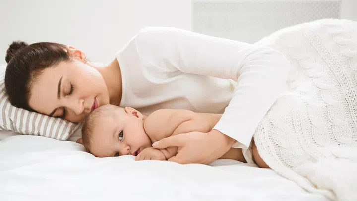 Baby is awake. Tired mom sleeping and embracing her little adorable kid who is already wake up, panorama