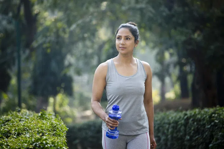 Fit woman running in sportswear with dumbbell shape water bottle at park