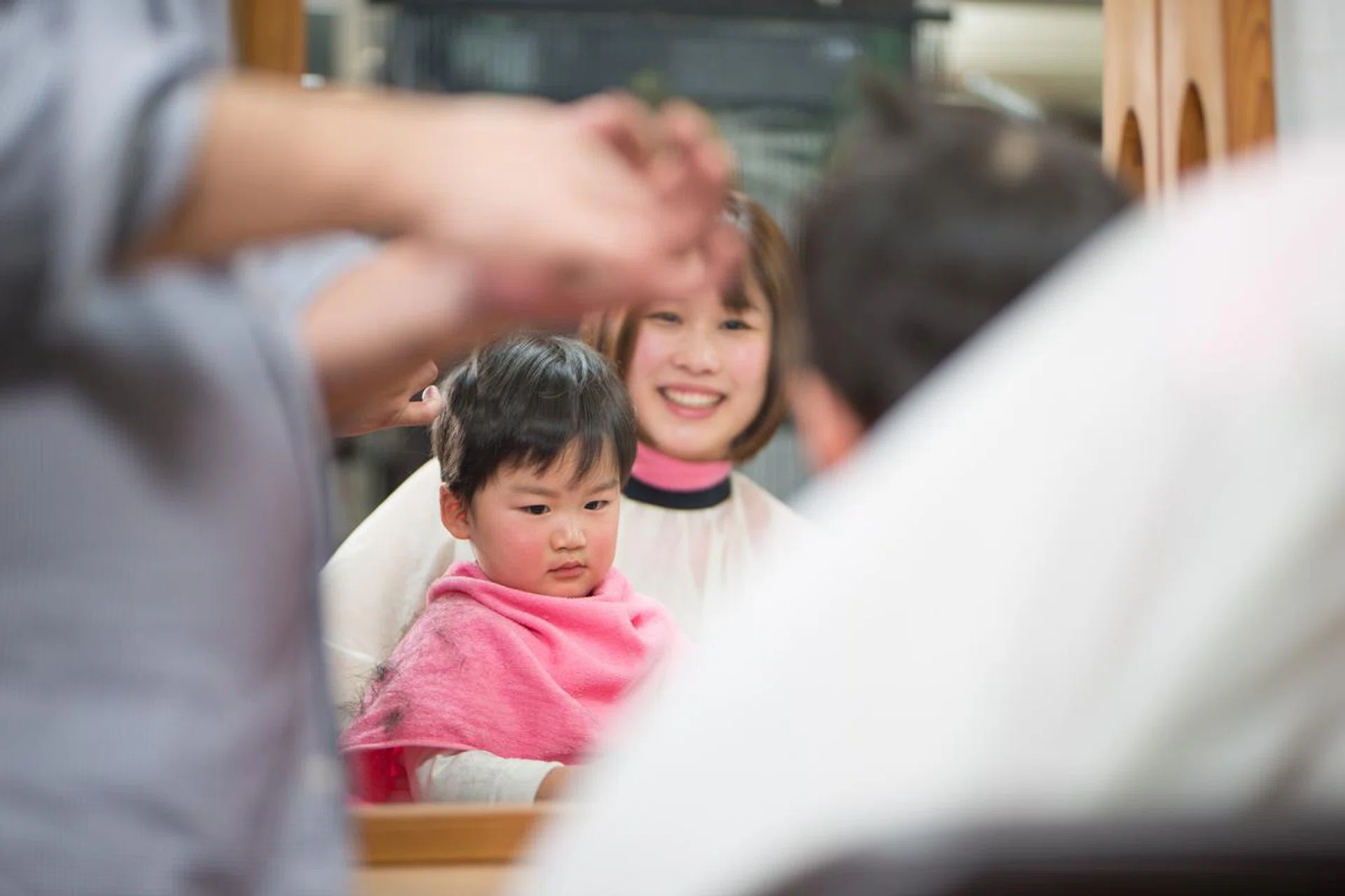 Child has his hair cut by hairdresser with mother