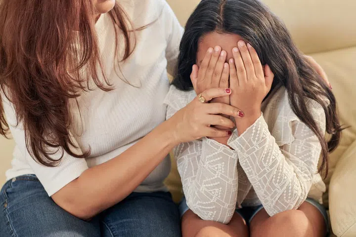 Mother trying to comfort her daughter covering face with hands and crying after being bullied in school