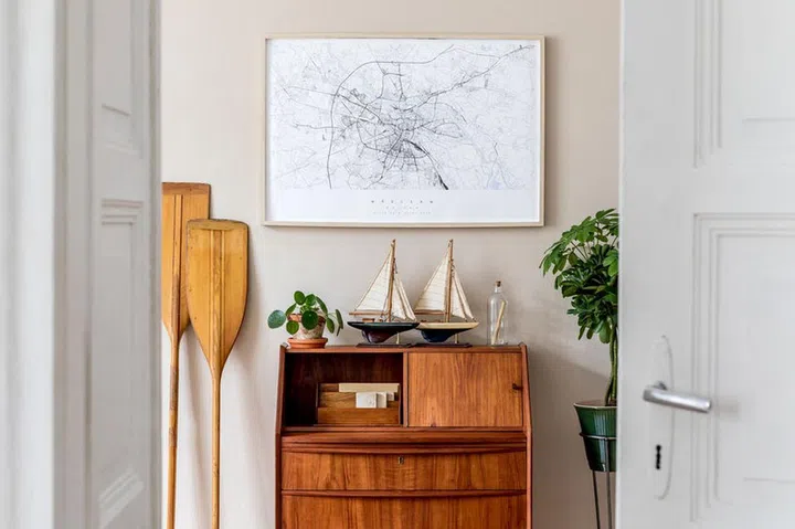 Stylish and vintage interior design of living room with wooden retro commode, plants, ships, paddle, map and elegant personal accessories. Mock up poster frame on the wall. Template. Home decor.