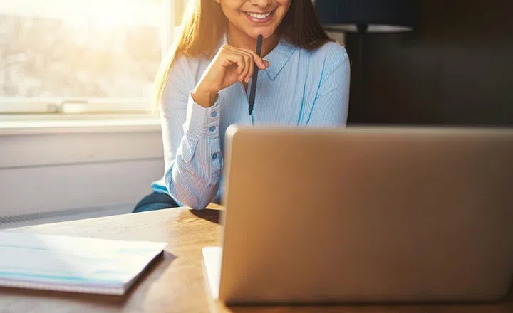 Business woman working at office looking at laptop with a pen in her hand