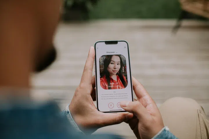 Close-up of a male holding a smart phone, and browsing a dating application. He looks at a photo of a woman.