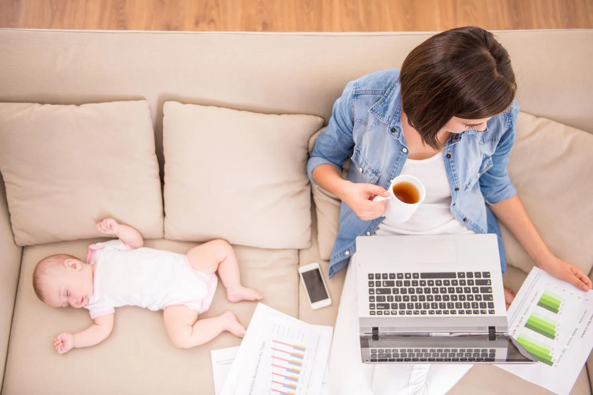 48108301 - top view of young woman is working at home and drinking tea while her little baby is sleeping.